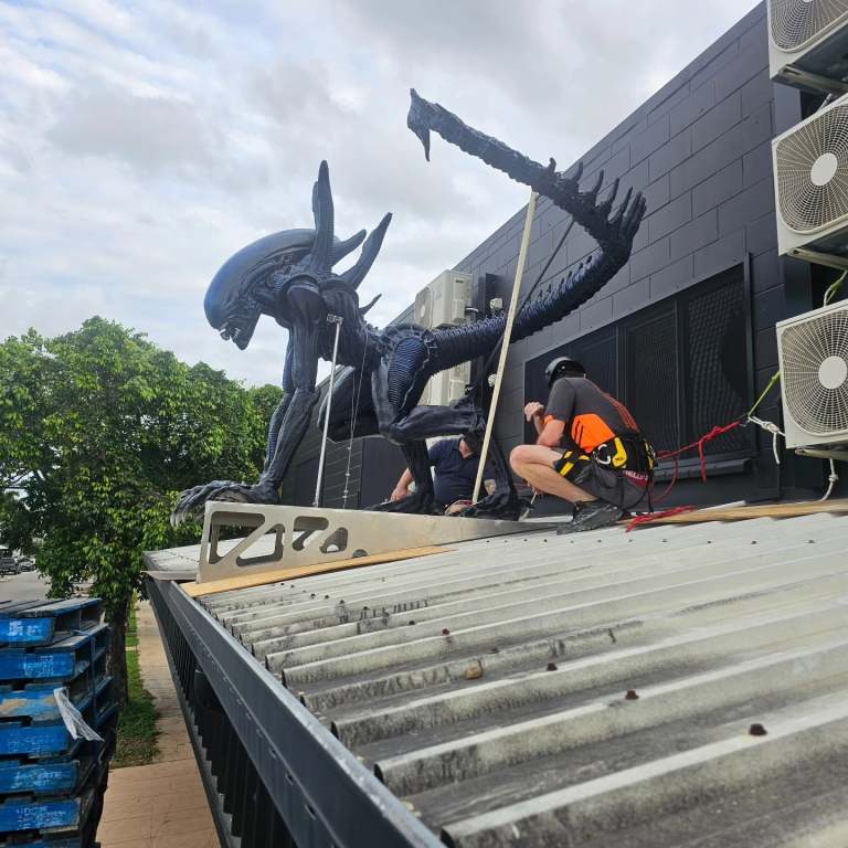 Workers in harnesses installing the 3D printed xenomorph on a rooftop