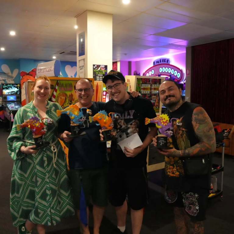 Pinball winners holding colourful 3D printed anglerfish trophies at Empire Altercade